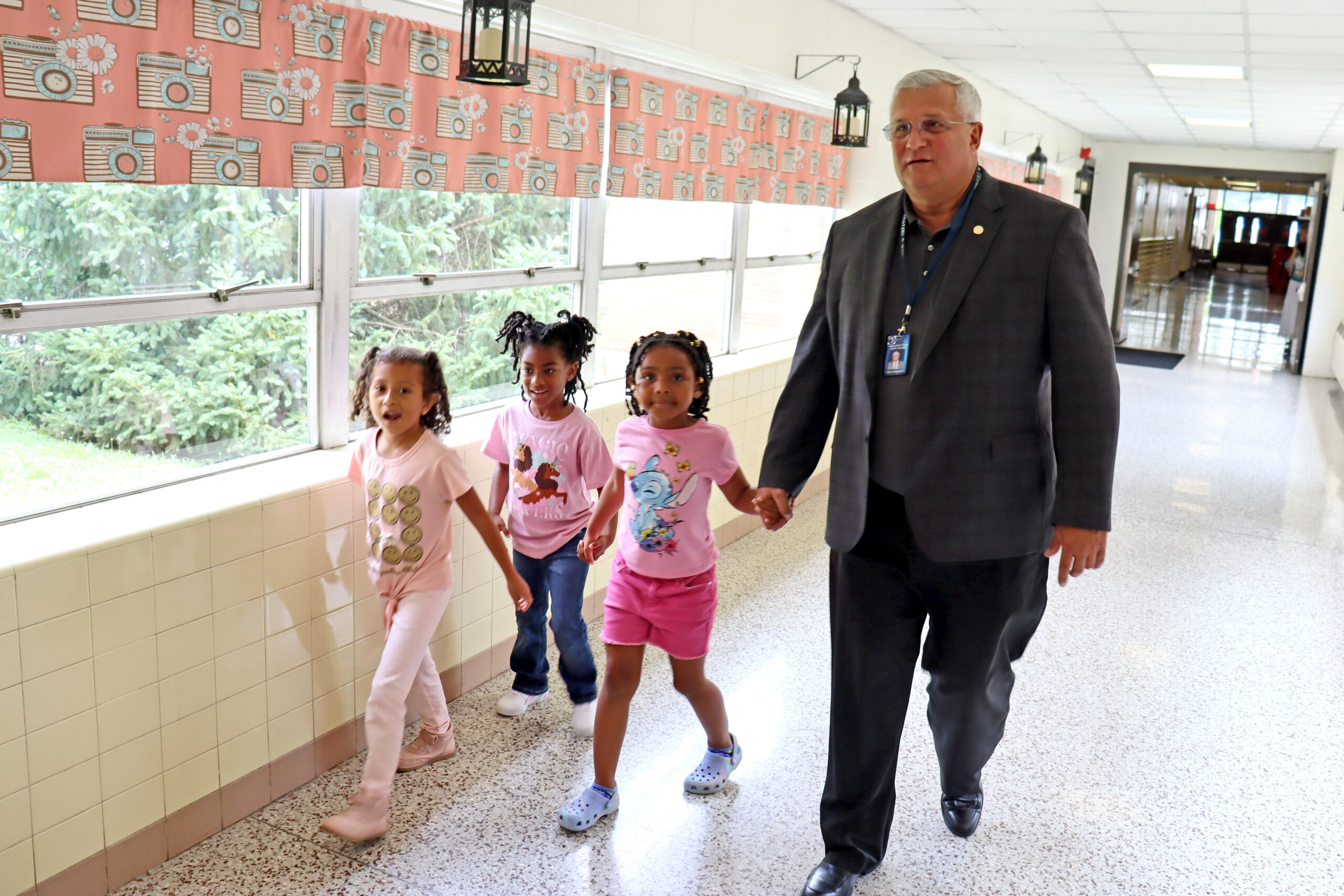 Dr. D holding hands with three students walking down hallway.