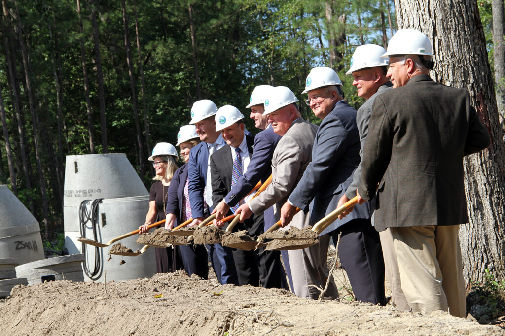 Multiple people shoveling dirt during a groundbreaking ceremony while wearing hard hats
