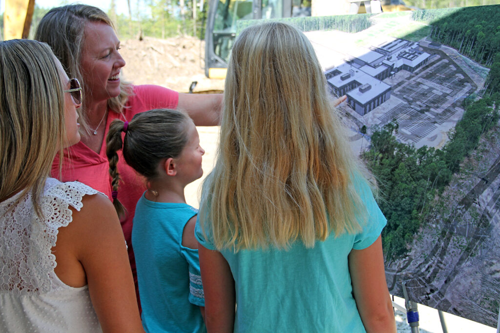 Two mothers and two daughters looking at an architect rendering of a new school