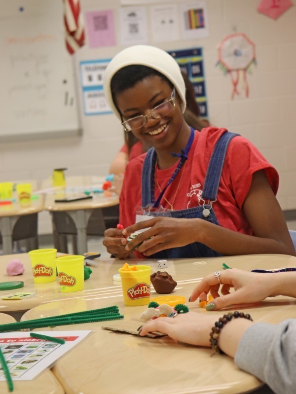 Student smiling and sculpting with Play Doh