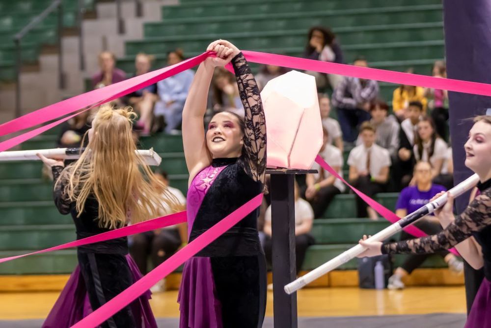 A student in a colourful dance outfit holding a ribbon above her head