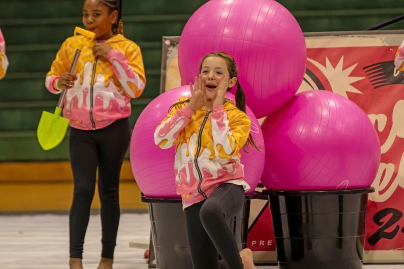 A young girl shouting in front of three large pink balls