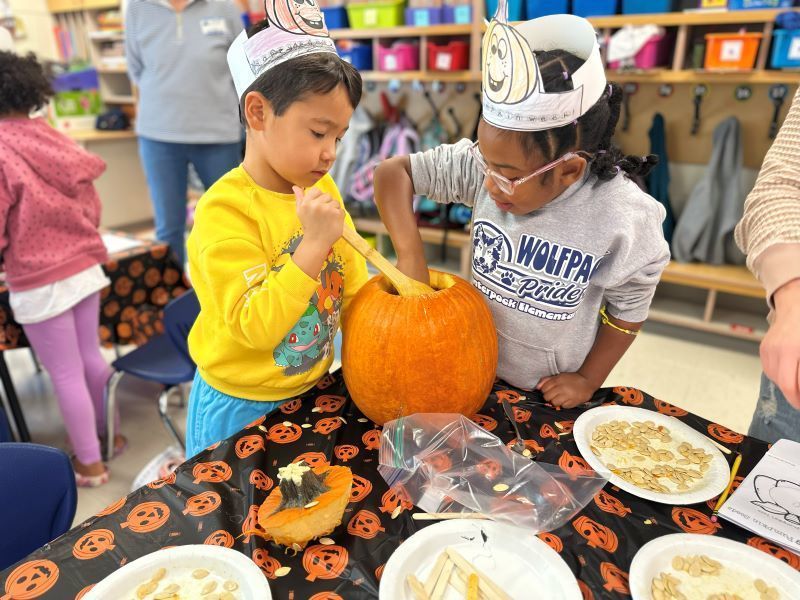 Two students pulling seeds out of a pumpkin