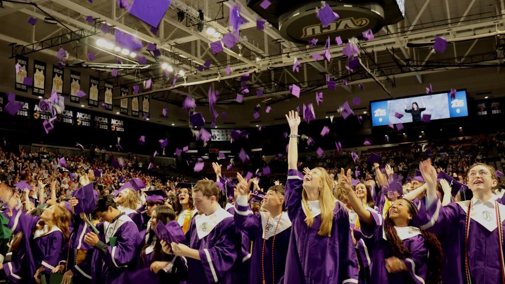Graduates in purple gowns tossing their caps