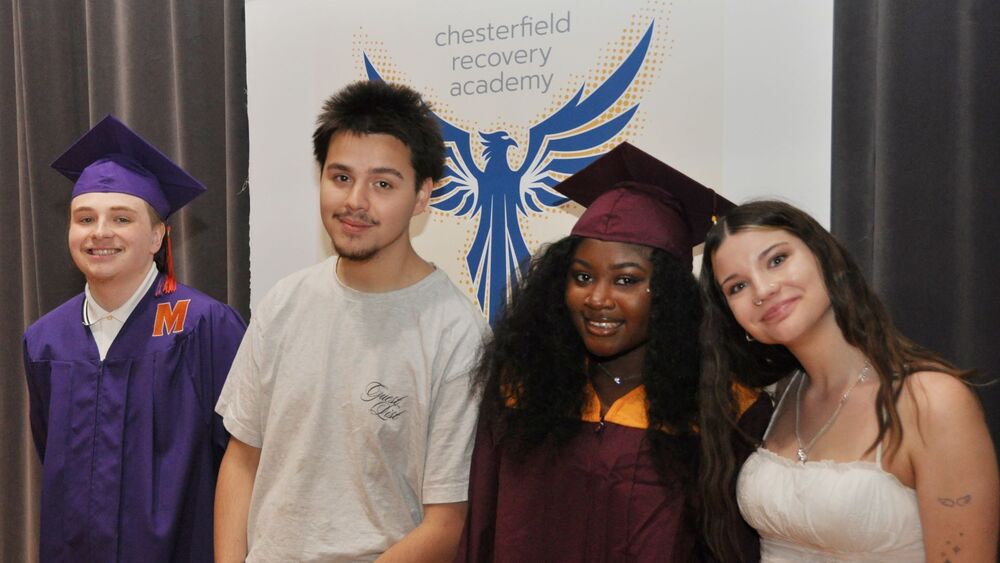 4 students smiling in front of the Chesterfield Recovery Academy phoenix logo
