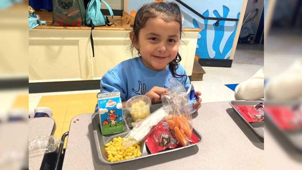 Young girl smiling with a meal on a cafeteria tray