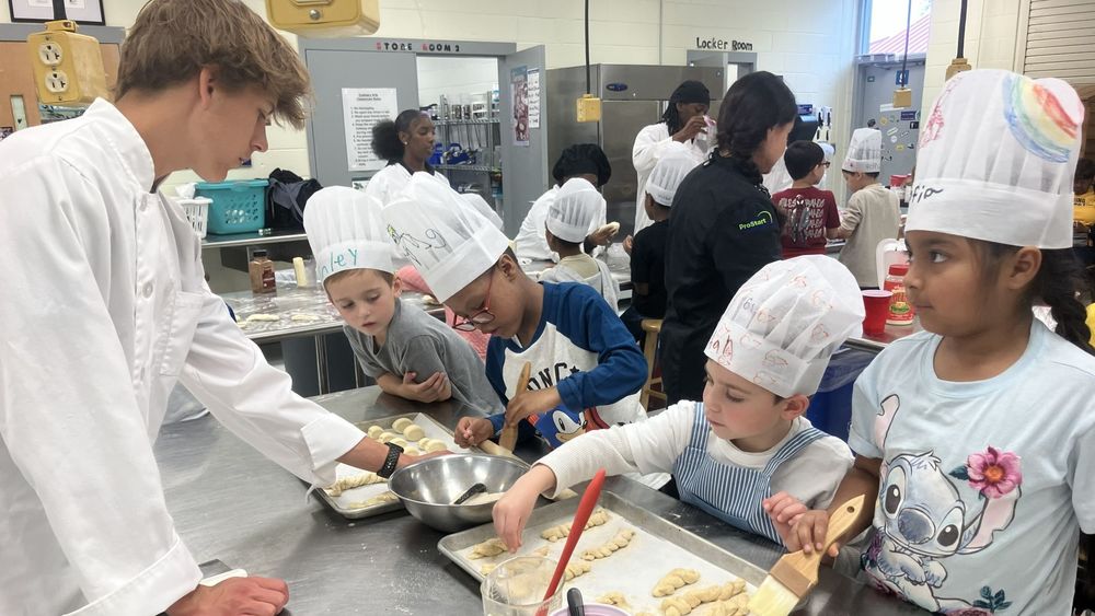 An older student working with younger students in chefs hats