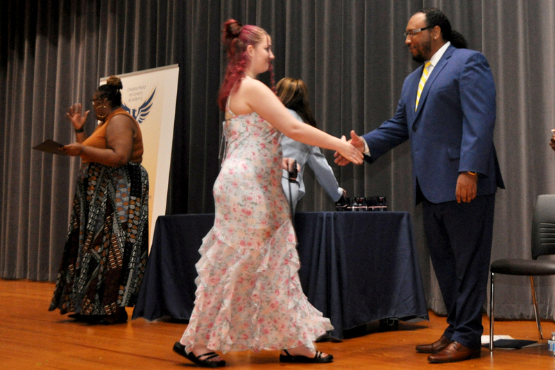 Student in a gown shaking an adults hand on stage