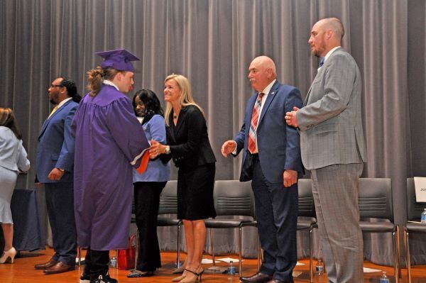 Student in a cap and gown shaking hands with Lisa Hudgins on stage
