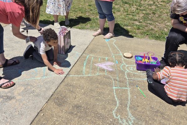 Students coloring a chalk drawing a of a student on the sidewalk
