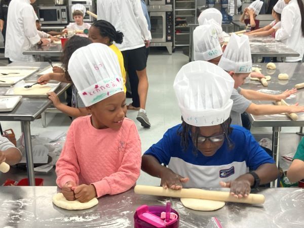 Two students in chefs hats rolling dough