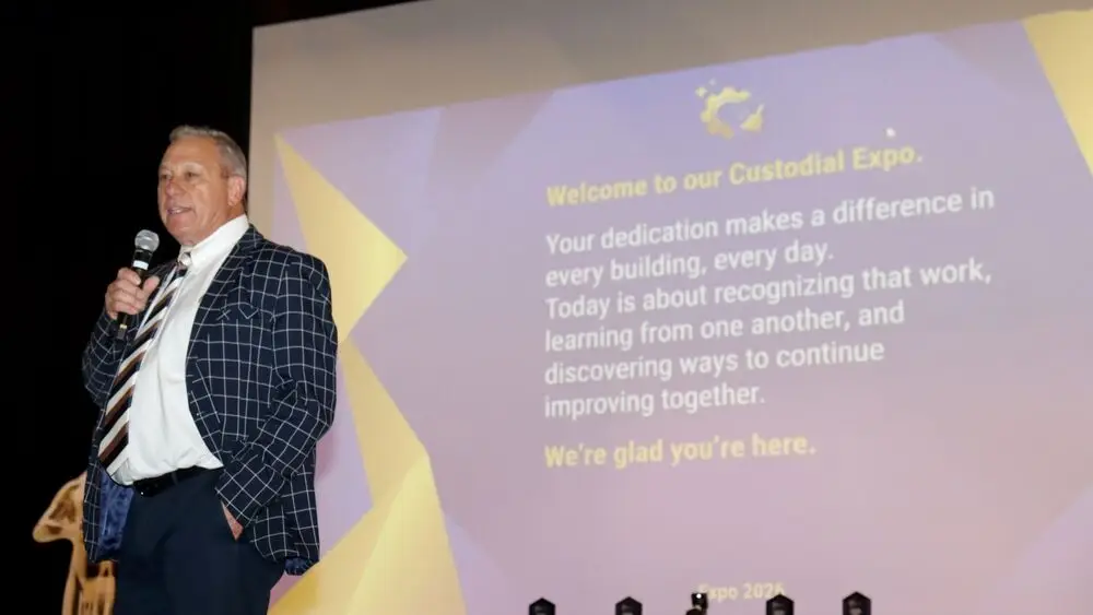 Man in a suit speaking in front of a welcome screen