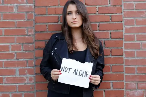 Woman holding 'Not Alone' sign by brick wall. Woman holding 'Not Alone' sign by brick wall.